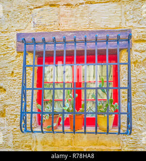 Die winzigen roten Fenster hinter den Bars und Kakteen in Töpfe mit Wohnhaus in Naxxar Stadt, Malta Stockfoto