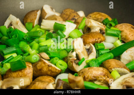 Nahaufnahme der gehackten grünen Frühlingszwiebeln und essbare Pilze in der Pfanne. Stockfoto