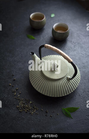 Teekanne und Teetassen auf schwarzem Hintergrund. Traditionelle asiatische Tee Set Teekanne und Teetassen Keramik mit grüner Tee und Kaffee verlässt. Stockfoto