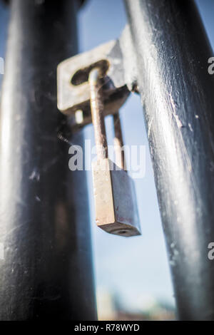 Ein Messing Vorhängeschloss auf einen Metallzaun, von einem niedrigen Winkel gesehen Stockfoto