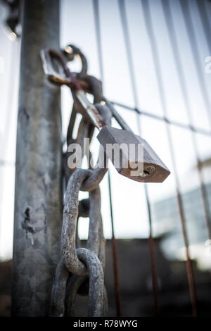 Ein Messing Vorhängeschloss auf einen Metallzaun, von einem niedrigen Winkel gesehen Stockfoto