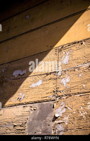 Gelbe Farbe Rissbildung und Ablösung der hölzernen Wand eines alten Gebäudes. Stockfoto