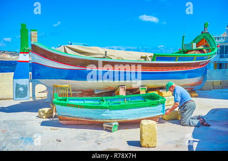 BUGIBBA, MALTA - 14. JUNI 2018: der Ältere Bootsmann Reparaturen und malt die alte hölzerne Beiboot am Ufer des Hafens, am 14. Juni in Bugibba. Stockfoto