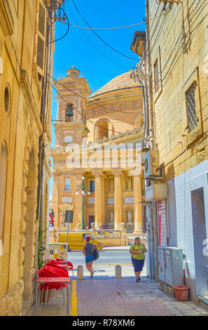 MOSTA, MALTA - 14. JUNI 2018: Der Blick auf den riesigen Basilika Rotunde durch die enge Gasse mit kleinen Cafe, am 14. Juni in Mosta. Stockfoto