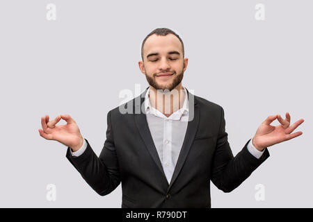 Ruhig und friedlich junger Mann in Anzug zu meditieren. Er hält die Augen geschlossen. Seine Hände sind seitlich vom Körper. Auf weissem Hintergrund. Stockfoto