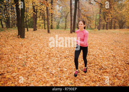 Glückliche junge Frau joggen außerhalb. Sie hören Sie Musik über Kopfhörer. Junge Frau lächelt. Sie läuft allein. Stockfoto