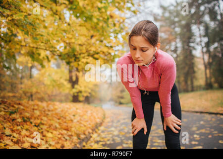 Gut gebaut aber müde Frau steht auf der Straße in den Park. Sie ist erschöpft. Frau hält die Augen geschlossen. Sie hören Sie Musik über Kopfhörer. Modell ist allein im Park. Stockfoto