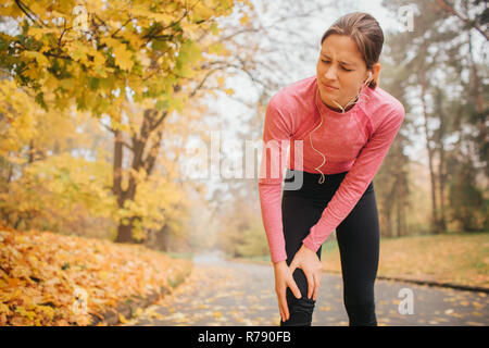 Schlank und gut gebauten jungen Frau steht auf der Straße im Herbst Park. Sie hält die Hände auf die Knie. Modell fühlt es den Schmerz. Sie leiden. Stockfoto