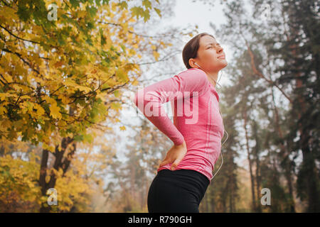 Junge Frau leidet unter Schmerzen im Rücken. Sie steht im Herbst Park und schauen Sie oben. Frau leidet. Stockfoto