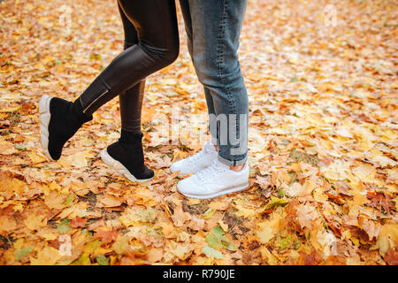 Cut vuew junger Mann und Frau Beine. Er steht auf zwei. Sie hält man die Füße hoch. Sie stehen auf gelbe Blätter. Stockfoto