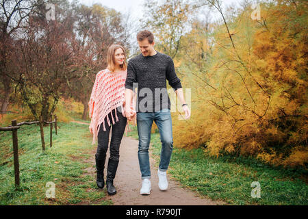 Junger Mann und Frau gehen gemeinsam in den Park. Sie halten einander die Hände. Stockfoto