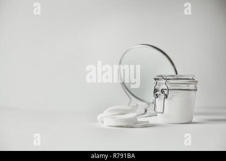 Schöne minimalistische konzeptionelle Alle weissen Komposition - Wattepads, transparente Jar und runden Spiegel, alles Weiß, mit metallischen Details Stockfoto