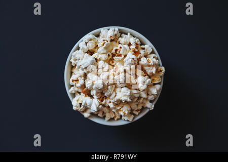 Eine Schüssel Popcorn auf dunklem Hintergrund in der Mitte platziert. Ansicht von oben. Stockfoto