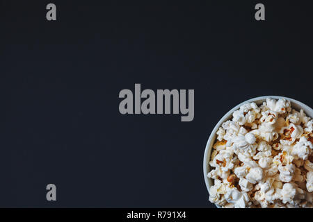 Eine Schüssel Popcorn auf dunklem Hintergrund in der rechten unteren Ecke beschnitten. Ansicht von oben. Stockfoto