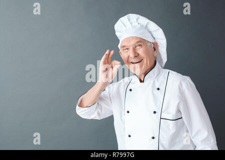 Senior Chef Studio stehen isoliert auf grau angezeigt ok Geste lächeln glücklich Stockfoto