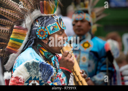 Ein Profil Portrait eines Südamerikanischen peruanischen Gaukler in farbenprächtigen, traditionellen Outfit gekleidet und Spielen auf der Panflöte für interessierte Zuschauer Stockfoto