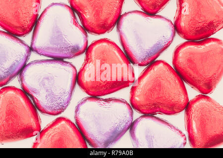 Mit einem Hintergrund von Schokolade oder Bonbons Herzen in rosa und rot Papier gewickelt und für die Liebe am Valentinstag als Geschenk oder mit Kopie bereit. Stockfoto