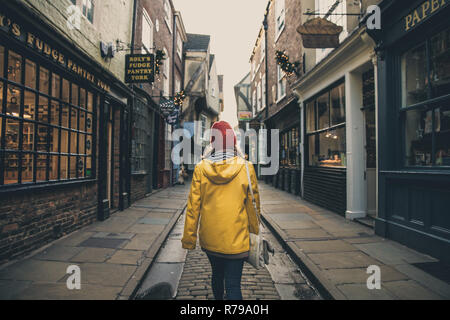 THE SHAMBLES, York, UK - 8. Dezember 2018. Eine modische junge Mädchen in einem gelben Mantel wandern entlang der mittelalterlichen Straße namens The Shambles in York, Großbritannien Stockfoto