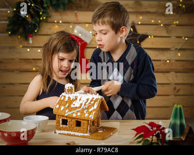 Foto von einem jungen Bruder und Schwester Dekorieren ein Lebkuchenhaus zu Hause kurz vor Weihnachten. Stockfoto
