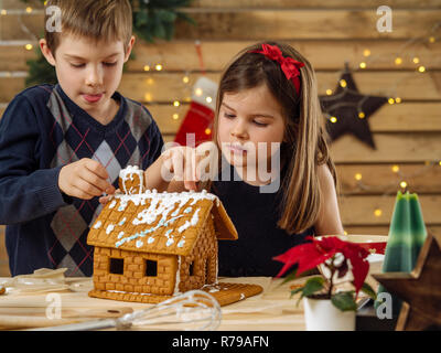 Foto von einem jungen Bruder und Schwester Dekorieren ein Lebkuchenhaus zu Hause kurz vor Weihnachten. Stockfoto