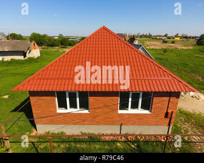 Haus mit einem orangefarbenen Dach aus Metall, Ansicht von oben. Metallische Profil gestrichen Wellpappe auf dem Dach. Stockfoto