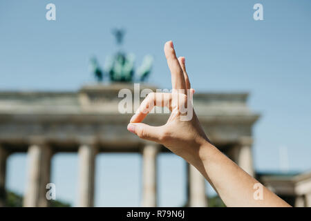 Eine Person zeigt ein Zeichen mit seinen Fingern, dass bedeutet, alles vor dem Hintergrund des Brandenburger Tor und blurry unkenntlich Menschen in Berlin in Deutschland gut ist. Stockfoto