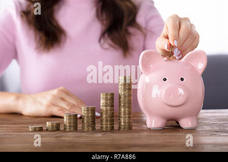 Frau einfügen Münze in Sparschwein in der Nähe von steigenden Gewinn Stockfoto