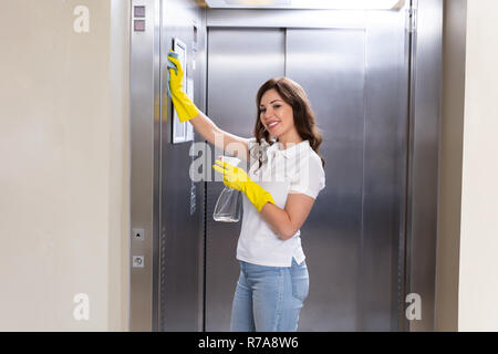 Seitenansicht eines lächelnden jungen weiblichen Hausmeister Reinigung Aufzug mit Duster Stockfoto