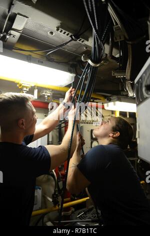 Seaman Jordanien Popovec (Links) und Petty Officer 3rd Class Catherine Desmarais (rechts) nach unten ziehen, um den Not-Aus-Kabel durch die Decke im Maschinenraum der Coast Guard Cutter Tiger Shark in Newport am Mittwoch, 12. April 2017. Desmarais, Maschinen Techniker, und Ihre shipmates ersetzt eine fehlerhafte Steuerbord Notbremse Draht, das die Motoren zum Stillstand bringt. Stockfoto