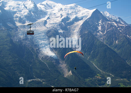 Ein Gleitschirm Piloten fliegen und die brevent Seilbahn vorbei vor der Mont Blanc und der Aiguille du Midi Gletscher, über Chamonix. Stockfoto