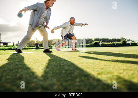 Menschen spielen eine Partie Boule in eine Wiese mit Sonne in den Hintergrund. Zwei ältere Personen nach vorne beugen Boule mit ihren Schatten auf dem Boden zu werfen Stockfoto