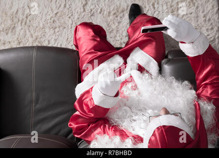 Overhead von Santa Claus (oder Kris Kringle) Entspannung im Sofa zu Hause mit Handy für Kommunikation und Freizeit. Ein videocall oder ein Selbst Stockfoto