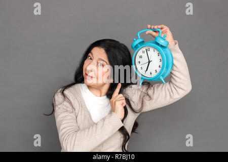Freestyle. Reife lady steht auf Grau shwoing Zeit auf Wecker isolierten Betroffenen Stockfoto