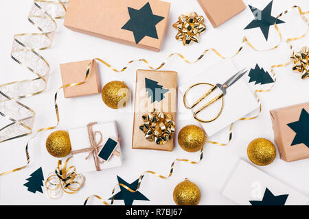 Festliche flach Anordnung der Verpackung Weihnachtsgeschenke mit den goldenen Bögen, Kartons, Papier - schwarze Sterne ausschneiden und Pinien auf weiße Tabelle, Ansicht von oben. Stockfoto