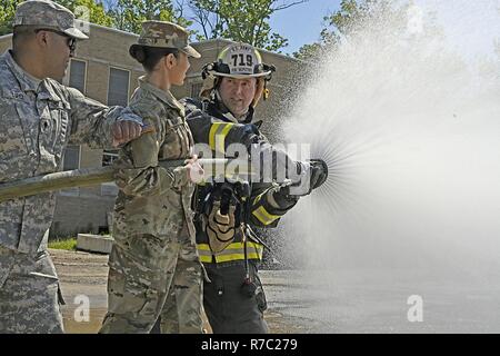 Der Soldat mit der Indiana National Guard 719th Engineer Feuerwehrmann Loslösung Sitz zeigt SPC. Roy Lopez der im Broadcast Operations Loslösung und Pfc. Anamarie Fajardo der 205th Drücken Sie Camp Headquarters, wie ein feuerwehrschlauch effektiv zu arbeiten während der Feuerwehrmann Ausbildung bei muscatatuck Urban Training Center, Mai 13. Stockfoto