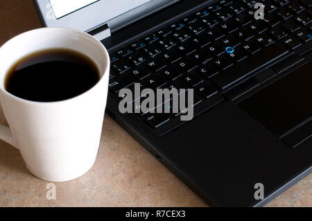 White Coffee Mug und Laptop Computer auf einem Tisch Stockfoto