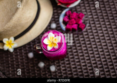 Red Dragon Obst im Glas dekoriert mit Plumeria Flower. Hut, Eiswürfel, Dragon Fruit über dunkle braune Oberfläche schneiden. Ansicht von oben. Stockfoto