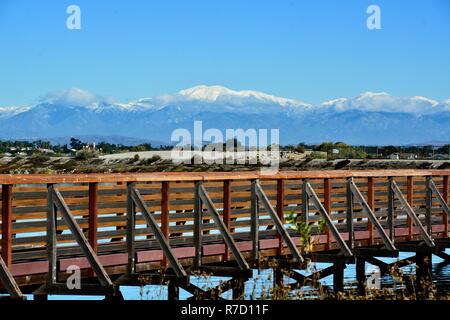 Hölzerne Brücke an der Bolsa Chica Feuchtgebiete in Huntington Beach, CA mit schneebedeckten Mt. Baldy im Hintergrund. Stockfoto