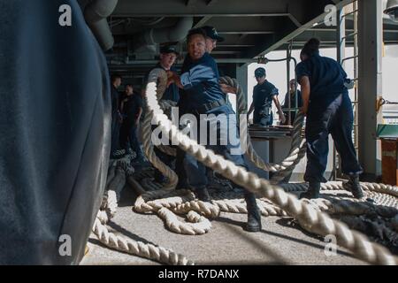 Singapur (Nov. 28, 2018) der Bootsmann Mate 3. Klasse Donye Wright, von Virginia Beach, Virginia, griffe Verankerungsleine auf der fantail an Bord der Nimitz-Klasse Flugzeugträger USS John C Stennis (CVN 74) wie das Schiff unterwegs erhält vom Changi Naval Base, Singapur, nach einem geplanten Hafen besuchen. John C Stennis unterwegs ist die Durchführung von Routineaufgaben in der US-Pazifikflotte Bereich der Operationen. Stockfoto