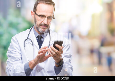 Mittleres Alter senior hoary Arzt Mann texting mit Smartphone über isolierte Hintergrund mit einem selbstbewussten Ausdruck auf Smart Face denken Ernst Stockfoto