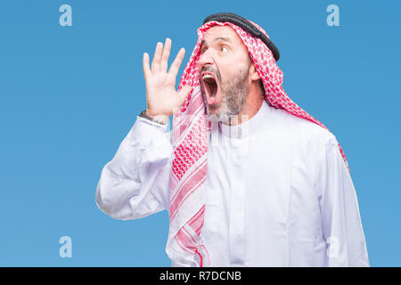 Senior arabischen Mann mit kufiya über isolierte Hintergrund schreien und schreien laut mit Hand auf Mund-zu-Seite. Kommunikationskonzept. Stockfoto