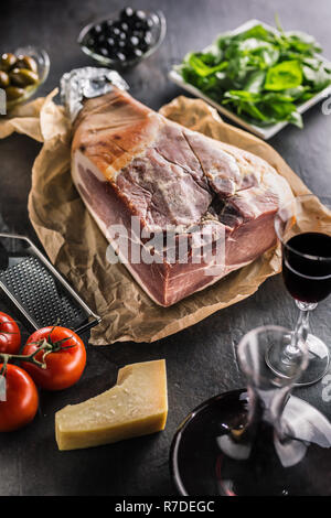 Schinken auf Tabelle mit mediterranen Zutaten - Oliven Tomaten Basilikum Parmesan und Rotwein. Stockfoto