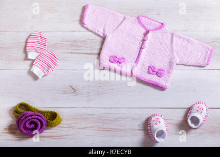 Baby Kleidung rosa Pullover Baumwolle gestrickt winzig kleine Handschuhe Socken auf weißem Hintergrund Holz, Kleinkinder Tuch auf den Tisch gesetzt, Kind neugeborene Mode clothi Stockfoto