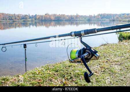 Karpfenruten sind auf der steht am Ufer gegen die flache Oberfläche des Sees mit einer Spule im Vordergrund installiert. Hintergrund. Stockfoto