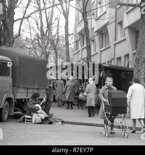 Leute einkaufen gehen auf einen wöchentlichen Markt während eines Behinderten banjo Player am Straßenrand im Viertel Montmartre in Paris sitzt, Frankreich, im November 1970. Foto: Wilfried Glienke | Verwendung weltweit Stockfoto