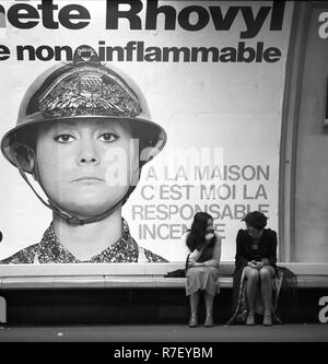 Zwei Frauen sitzen im Rahmen einer Werbung für synthetische Textilien und sprechen, in Paris, Frankreich, im November 1970. Die Werbung lobt die Brennbarkeit des Materials. Der Slogan lautet: "Zu Hause, ich bin für die feuersbrunst verantwortlich." Foto: Wilfried Glienke | Verwendung weltweit Stockfoto