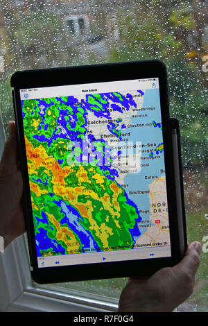 Frau Hände halten des ipad pro Tablette regen Alarm app nutzt Echtzeit Farbe radardaten überlagernden Niederschlag auf der lokalen Karte regnerische Wetter auf Fenster Essex UK Stockfoto
