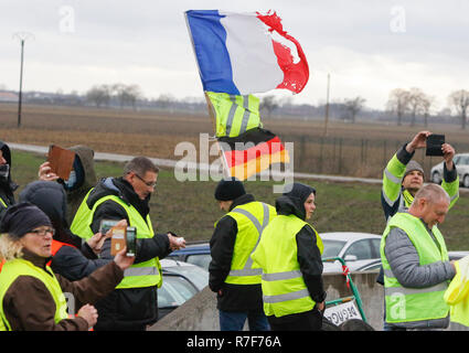 Roppenheim, Frankreich. 08 Dez, 2018. Die demonstranten stehen auf der Seite der Straße. Eine Demonstrantin trägt eine französische und eine deutsche Flagge. Rund 100 Französische gelbe Weste Aktivisten protestierten auf einer Straße in der Nähe der Französisch Deutsch Grenzübergang bei Roppenheim gegen die französische Regierung. Sie wurden von einigen Aktivistinnen aus der Deutschen rechten Gruppen unterstützt. Sie waren Teil der grösseren gelbe Weste Protestbewegung in Frankreich, die in den vergangenen 4 Wochen in ganz Frankreich protestiert. Quelle: Michael Debets/Pacific Press/Alamy leben Nachrichten Stockfoto