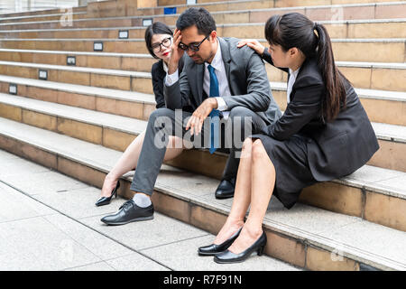 Eine traurige suchen junge Unternehmer sitzen auf der Treppe nach unten mit betont und schauen Geste gedrückt mit zwei geschäftsfrauen sitzen auf beiden Stockfoto