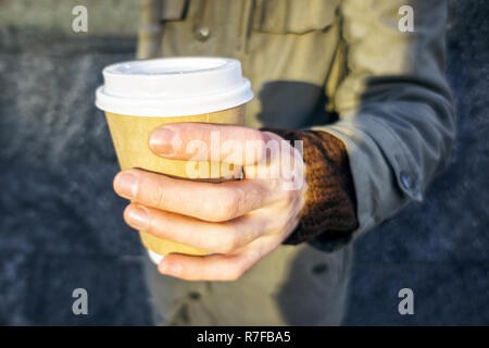 Papier heiße Tasse Kaffee in der Hand eines Mannes in einer Jacke und einer schwarzen Pullover. Wärmendes Getränk in der kalten Winter. Kaffee Konzept Stockfoto